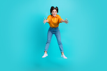 Full length photo of friendly impressed woman dressed orange shirt holding arms huge object jumping high isolated teal color background