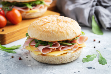 Two homemade sandwiches with ham, cheese and arugula on a concrete table.