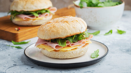 Two homemade sandwiches with ham, cheese and arugula on a concrete table.
