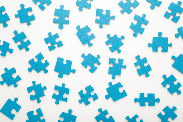 Different many blue puzzle pieces on white table background. Closeup. Top down view. Jigsaw pattern.