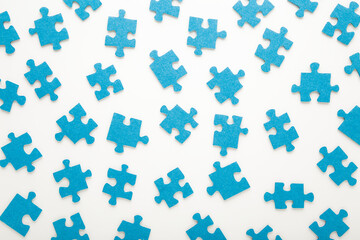 Naklejka premium Different many blue puzzle pieces on white table background. Closeup. Top down view. Jigsaw pattern.