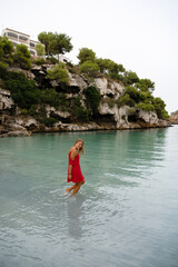 Young woman in red dress in the water in cala pi in Mallorca Spain