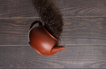 Fototapeta premium Black dried leave Tea fly in Pot. Small Fine size tea leaf flying explosion, Abstract cloud fly. Brown colored Teas pot splash throwing in Air. Wooden background Isolated high speed freeze