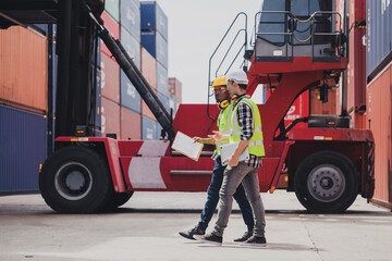 Cheerful Caucasian engineer wearing safety vest standing by shipping container terminal talking discussing information to African collaborator. Transportation business. Logistic industrial concept