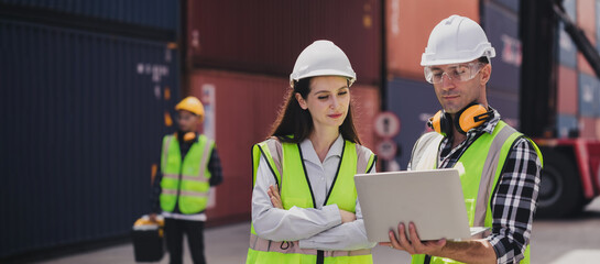 Cheerful Caucasian engineer wearing safety vest standing by shipping container terminal talking...