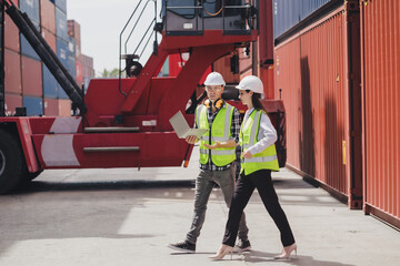 Cheerful Caucasian engineer wearing safety vest standing by shipping container terminal talking discussing information on computer to collaborator. Transportation business. Logistic industrial concept