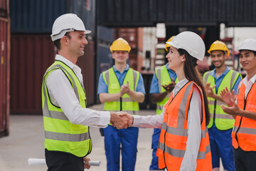 Caucasian engineer wearing safety vest standing by shipping container terminal and shake hand with collaborator. Transportation goods business in the shipping yard. Logistic industrial concept
