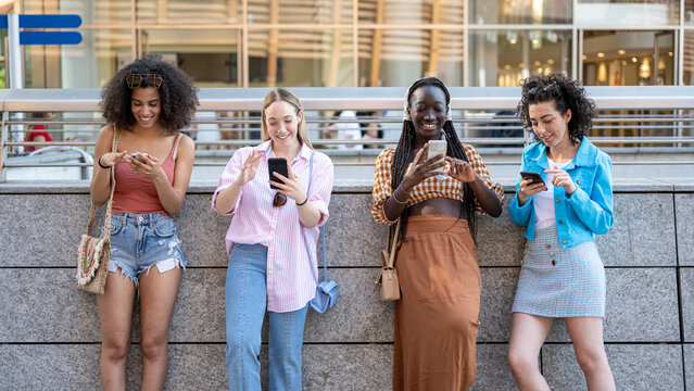 Four girls looking at their smart phones for checking social media and network, happy people of generation Z addicted to new technology and digital socialization
