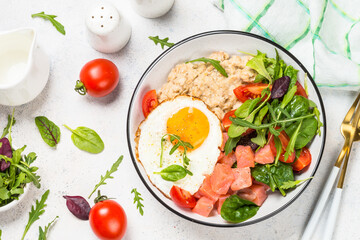 Savory breakfast. Oatmeal porrige with salted salmon, egg and fresh salad. Healthy food, balanced nutrition. Top view on white table.