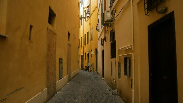 A walk in a narrow alley with cobblestone ground in the historical centre of Rome, Italy. Yellow walls at both sides.