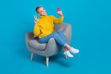 Fototapeta na wymiar Photo of positive lady sit comfort chair recording video streaming broadcasting show followers v-sign isolated on blue color background