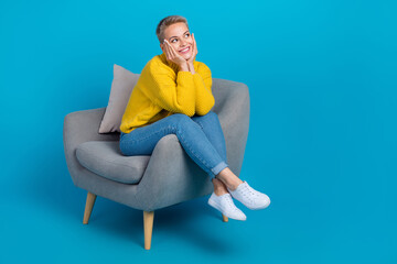 Fototapeta na wymiar Full size photo of dreaming sit comfortable armchair sofa blonde hair lady touch cheeks look empty space good news isolated on blue color background