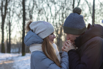 Fototapeta na wymiar Careful young man warming his girlfriend hands in winter park
