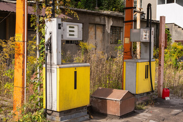 Old rusty gas station and dispensers abandoned and overgrown with vegetation on a sunny day. Summer.