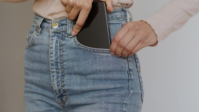 Close up of unrecognizable slim woman putting her modern smartphone into jeans pocket, slow motion, free space
