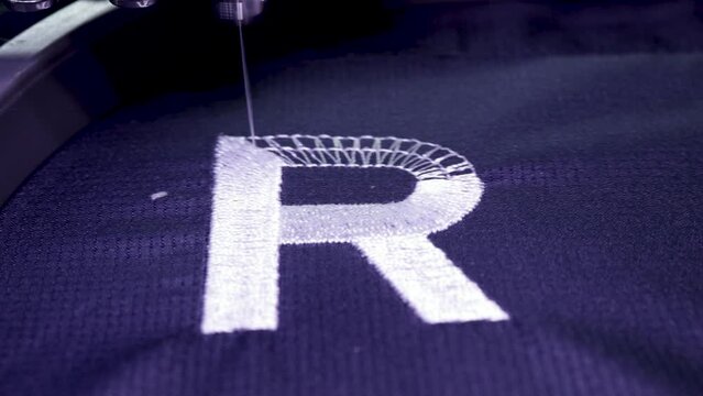 Machine embroidery of the inscription Russia on a blue T-shirt with white thread. Selective focus.