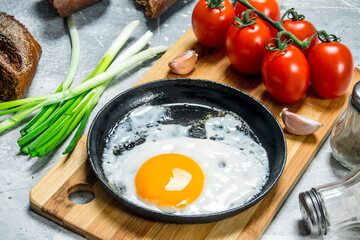 Fried egg in a pan with tomatoes and green onions.
