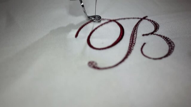 Machine embroider the inscription "B" on a white satin robe.
Inscription bride with burgundy thread. Wedding day preparation. Elegant bridal lingerie. Close up. Full Hd Video.