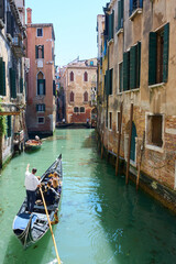 Fototapeta na wymiar View of narrow canal in Venice, Italy, with gondolier giving people a gondola ride surrounded by picturesque old houses.