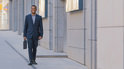 African American man ethnic smiling happy businessman employer entrepreneur boss leader worker investor lawyer male guy company CEO manager in business suit with suitcase walking in city walk outdoors