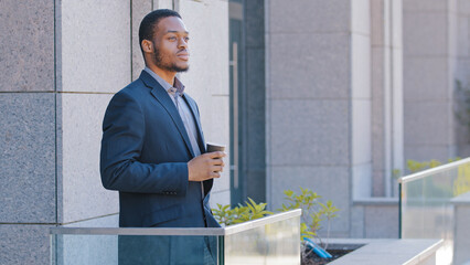 African American businessman pensive relaxed thoughtful entrepreneur office worker manager man guy male employer standing on balcony pondering business strategy think with tea coffee thinking relaxing