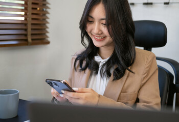 Fototapeta na wymiar Young business woman on the phone at office. Business people texting on the phone and working on laptop.Pretty young girl sitting on workplace. Joyful asian woman smiling while working in office.