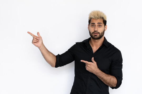 Amazed young man pointing with fingers at copyspace. Male Caucasian model with brown eyes, ombre painted hair and beard in black shirt presenting advertisement. Advertising concept