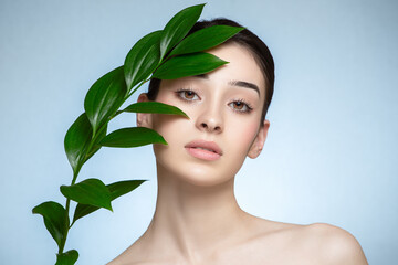 Portrait of woman and green leaves. Organic beauty. Blue background. - 561839966