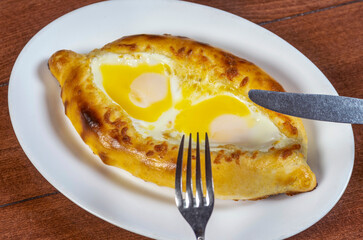 Man eating adjar Khachapuri. Georgian national pie khachapuri with egg and cheese in the white plate  on wooden background.