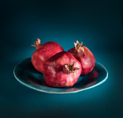 Still life with three red Pomegranate fruit on a plate at the tidewater green background, close-up