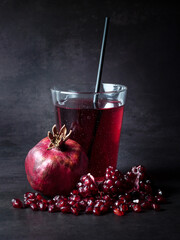 Pomegranate juice in a glass and pomegranate fruit on the table at black background.