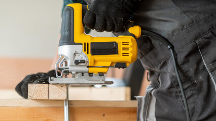 Close-up of a man cutting a wooden plank with an electric jigsaw in a workshop.