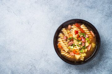 Vegetable soup with pasta and sausages. Top view with copy space at light stone table.