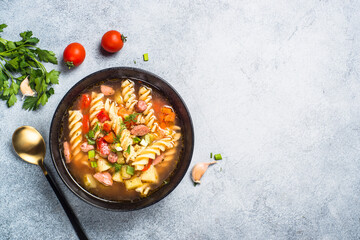 Vegetable soup with pasta and sausages. Top view with copy space at light stone table.