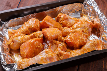 chicken drumsticks in sauce and spices marinated on foil on a baking sheet on a wooden table.