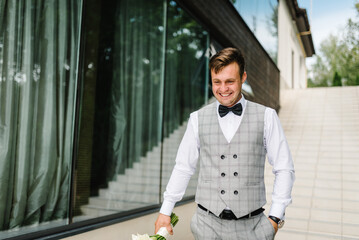 Groom waiting for his bride. A young man in suit holding bouquet of flowers and stand on the terrace, backyard. First meeting.