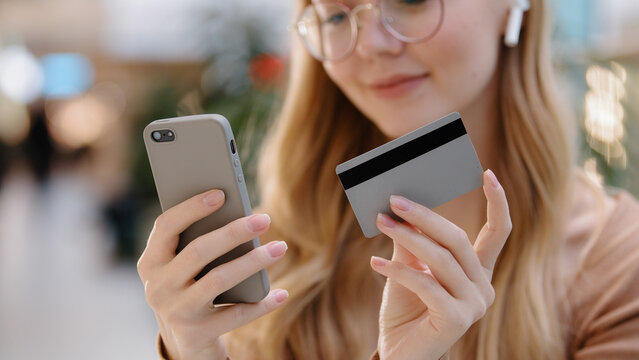Close-up young girl hands holding smartphone and credit card happy woman customer make online purchase pay bills using banking app on phone virtual remote shopping successful safe transaction concept