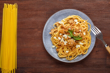 Homemade bolognese pasta on a plate on a wooden table next to a fork on a plate.