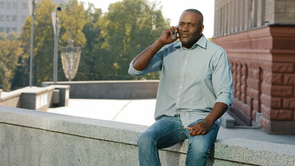 Adult mature African American man sitting outdoors holding cell phone angry middle-aged ethnic male...