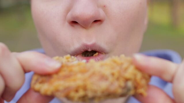 Satisfied young woman eating fatty crispy fried chicken, appetite, close up