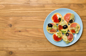 Tartlets with salmon and caviar on wooden background, top view