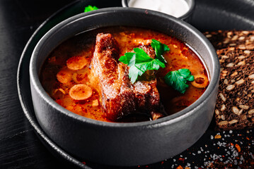 Solyanka soup with meat, sausage, vegetables, olives and lemon in bowl on wooden table background