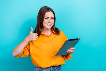 Photo of confident sweet lady wear orange shirt typing modern device thumb up empty space isolated turquoise color background