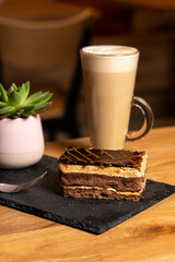 Latte coffee with chocolate caramel cake on wooden table in coffeeshop on black platter