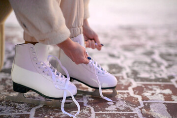 Women's hands tie shoelaces on white ice skates in winter.