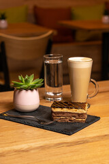 Latte coffee with chocolate caramel cake on wooden table in coffeeshop on black platter