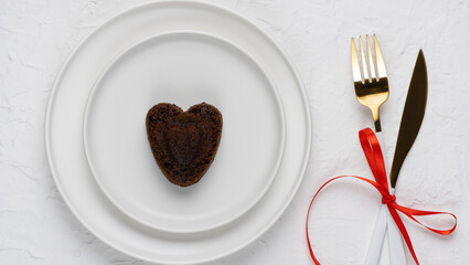 Heart shaped chocolate chip cookie on a white plate with a knife, fork and red ribbon