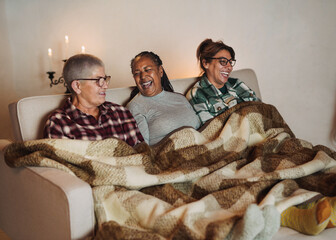 Elderly multiracial women having fun together sitting on the couch with blanket