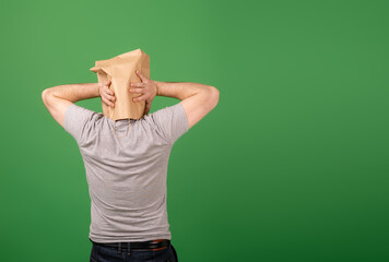 An unrecognizable man with a paper bag on his head grabbed his head against a green background....