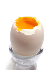 Close-up of one soft half-boiled egg. It is on a stand, isolated on white background. The top is open like a lid and shows delicious orange yolk. Called "Oeuf a la coque" in French.